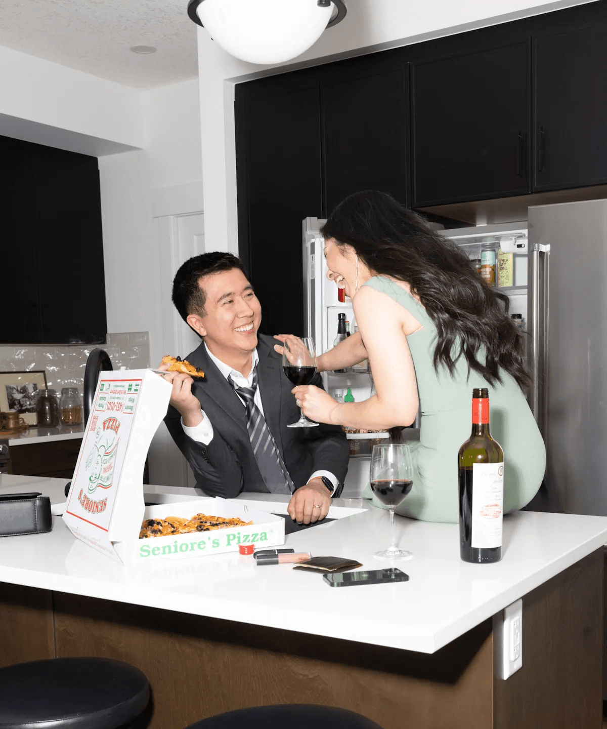 dressed up couple happily eating pizza and drinking wine in kitchen